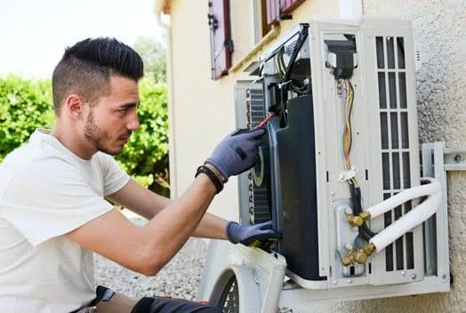 Technician inspecting a wall-mounted outdoor air conditioning unit